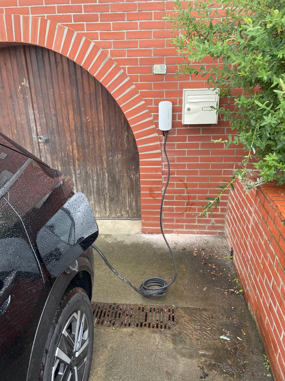 Borne de recharge murale posée sur une façade en brique, voiture électrique en charge
