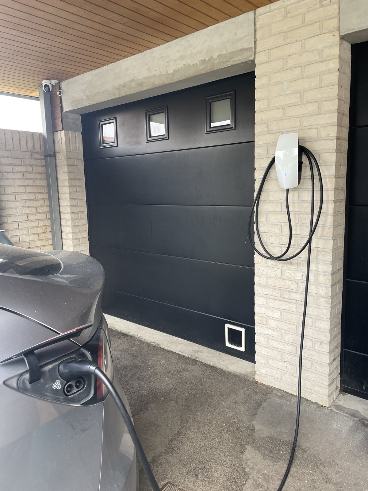 Borne de recharge murale installée à domicile, véhicule électrique en charge devant un garage